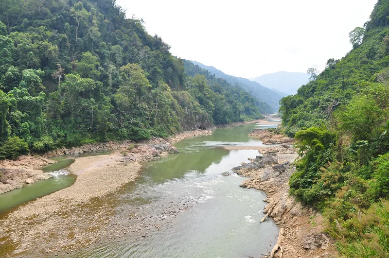 A winding river flows between forested mountains and rocky sandbars at the upper Da River in Lai Chau.