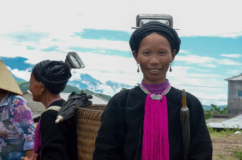 Women in traditional ethnic dress with distinctive headpieces smile in a mountain village in Lai Chau, Vietnam.