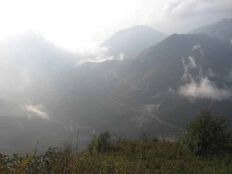 A winding mountain road snakes through misty peaks at O Quy Ho Pass in Lai Chau.