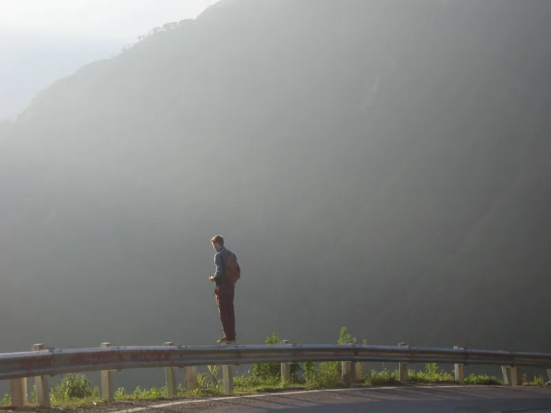 A traveler stands on a guardrail overlooking misty mountains at O Quy Ho Pass in Lai Chau.
