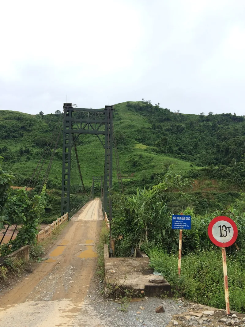 A green steel suspension bridge crosses a river surrounded by lush hills near Nam Khao, Lai Chau province.