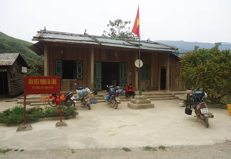A wooden border guard station with a Vietnamese flag and parked motorbikes in the mountains of Lai Chau.