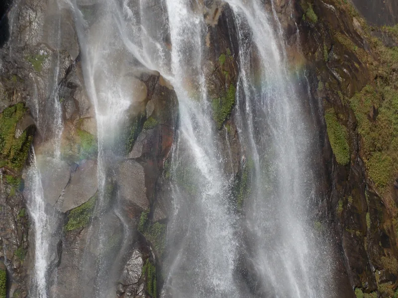 Cascading streams of a waterfall over mossy rocks with a faint rainbow in Lai Chau province, Vietnam.