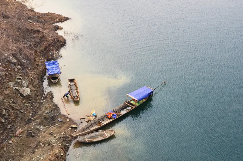 Wooden boats moored along a muddy bank of the Da River in Lai Chau, seen from above.