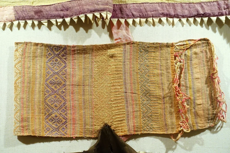 A handwoven Lao ethnic shoulder scarf with striped patterns and fringe, displayed at a museum in Lai Chau.