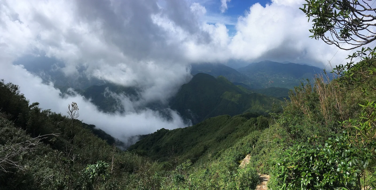 Clouds drift through green mountain ridges along a trail in the Hoang Lien Son range, Lai Chau.