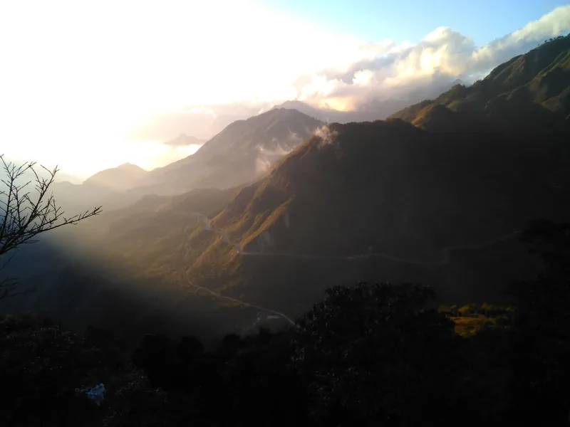 Sunset light breaks through clouds over the winding mountain road of O Quy Ho Pass in Lai Chau.